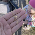 Collier personnalisé doré représentant un dessin d’enfant tenu dans une main, enfant flou en arrière-plan